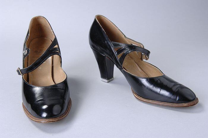 Zwarte lakleren hakschoenen, wreefband splitst naar de schoenwand toe in drie bandjes, siergesp met…