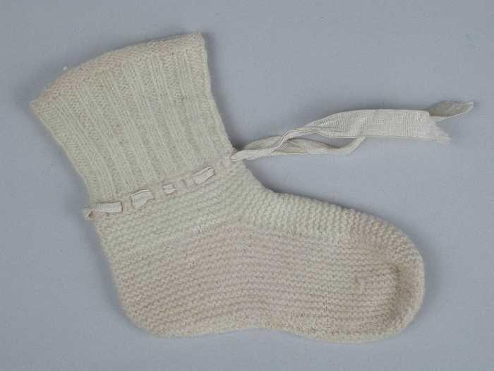 Paar babysokken gebreid van zachtroze en witte wol in tricot- en ribbelsteek, wit zijdelint door de…