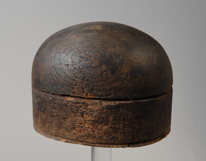 Hoedenmal van donkerkleurig hout bestaande uit een boven- en onderdeel, onder drie gaten, "56 1/2"