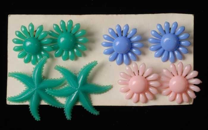 Vier paar oorbellen, clips met plastic bloemen en zeesterren in groen, roze en blauw, op karton,…