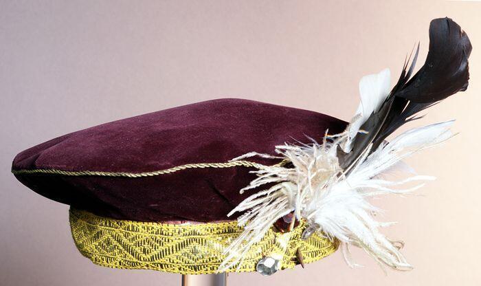 Auberginekleurige fluwelen ronde baret, zwarte pietenpet, met goudlamee band en garnering van twee…
