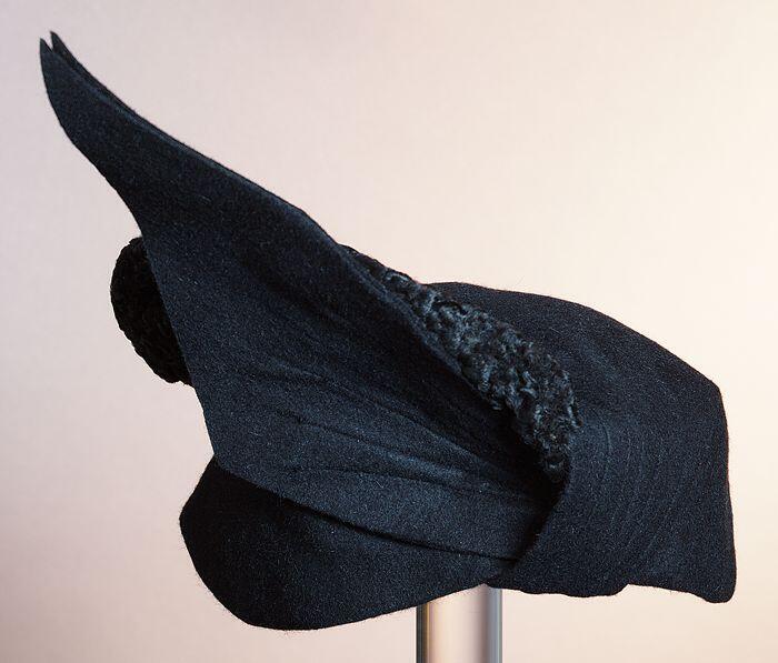 Zwart vilten dameshoed, asymmetrisch met opstaande flap, bol deels met imitatie astrakan bezet