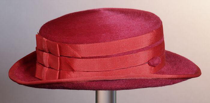 Dameshoed van rood fluweel, met rand, buitenste rand en bol afgezet met rood lint, bij bol achterin…