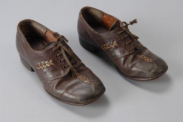 Bruine leren kinderschoenen met vetersluiting, op de neus en de zijkanten een ingevlochten…