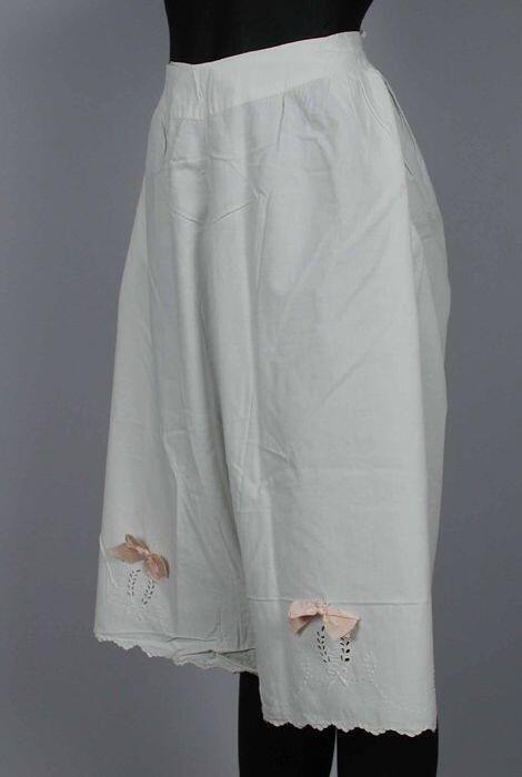 Witte katoenen onderbroek met pijpen versierd met broderie anglaise en zalmroze strikken,…