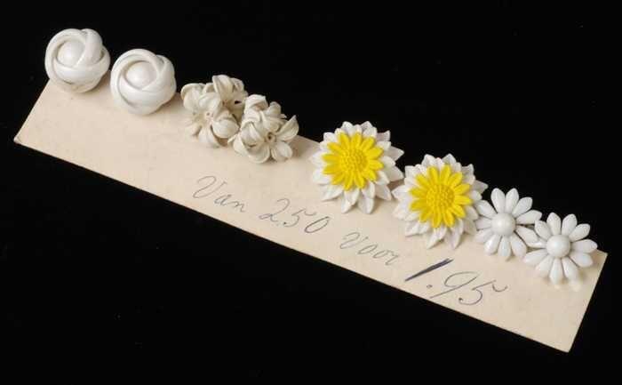 Vier paar verschillende oorbellen, clip met witte plastic bloemen, op strook karton, kapper Van…