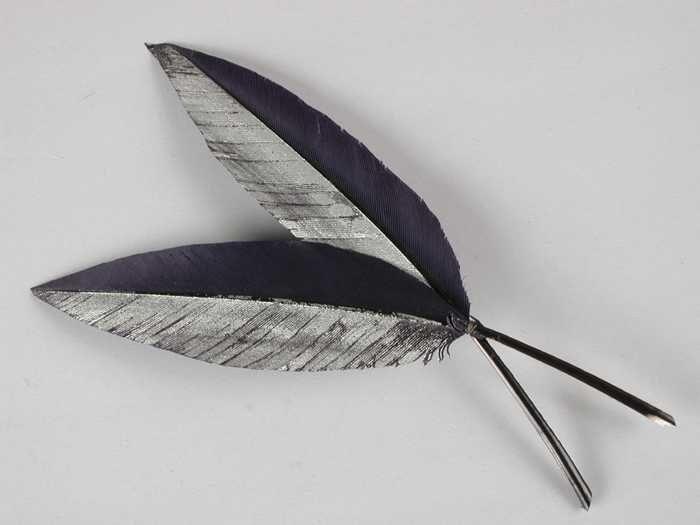 Verendecoratie, twee donkerblauw geverfde veren aaneengezet, één helft van iedere veer…