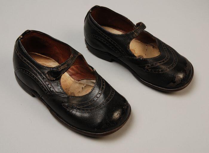 Paar kinderschoenen van zwart lakleer met wreefbandje met knoopsluiting en perforatie decoratie op…