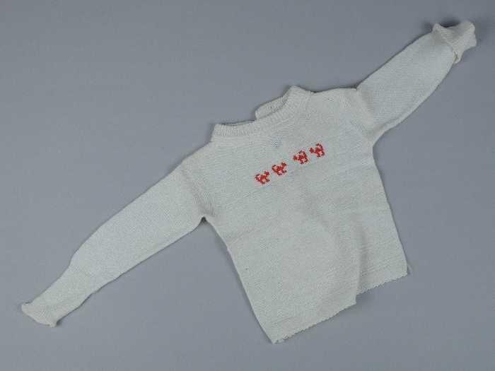 Babytrui gebreid van wit katoenin reliëf, lange mouwen, middenachter open, voorzijde in rood…