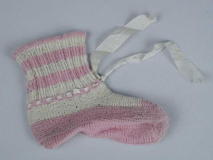 Paar babysokken gebreid van lila-roze en witte wol in tricot- en ribbelsteek, wit zijdelint door de…