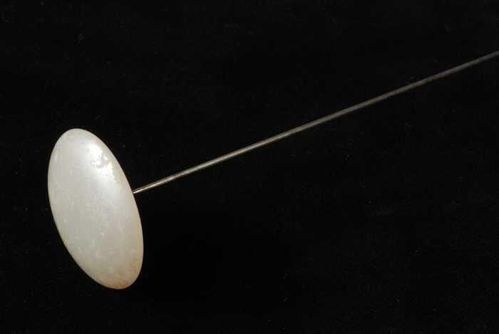 Hoedenspeld, lange metalen pen met scherpe punt, bolronde sierknop van wit matglas(?) met parelmoer…