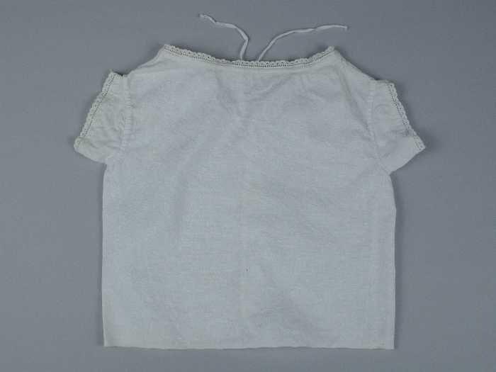Babyhemd van wit linnen smalle rand broderie anglaise langs hals en korte mouwen, koordje door…