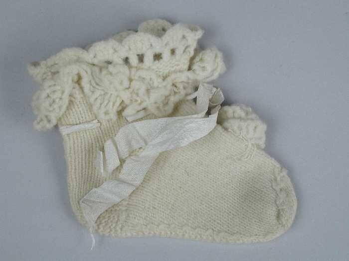 Paar babysokken gebreid van crèmekleurige wol in tricotsteek, zijdelint door de enkel, gehaakte…