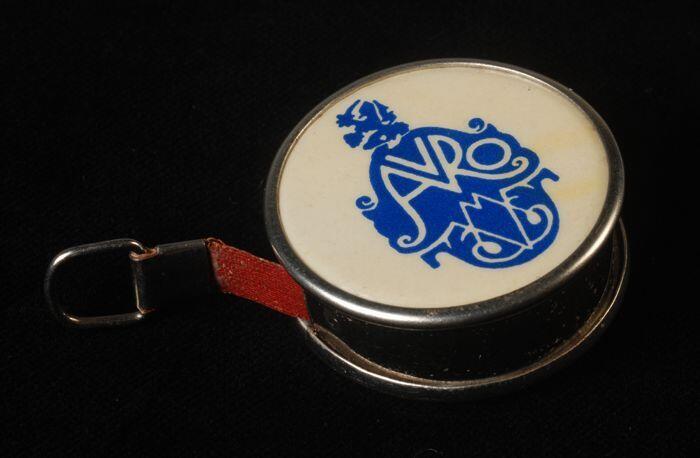 Rolcentimeter in ronde blank metalen huls met opschrift "Met Naald en Schaar. 25 jaar . AVRO"