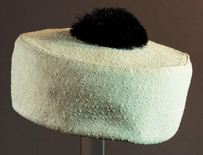 Pillbox van witte stof, zwarte raffia kunststofpompon midden op de platte bol