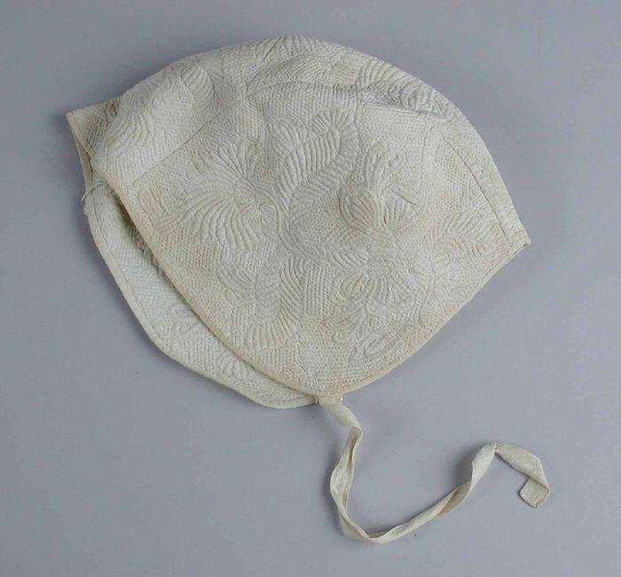 Kindermuts van crèmekleurig linnen drie panden met Zaans stikwerk in florale motieven, één strikband