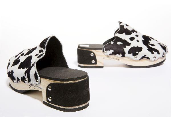 Een paar houten klompen bekleed met wit suèdeleer met zwarte flockprint in koeienmotief