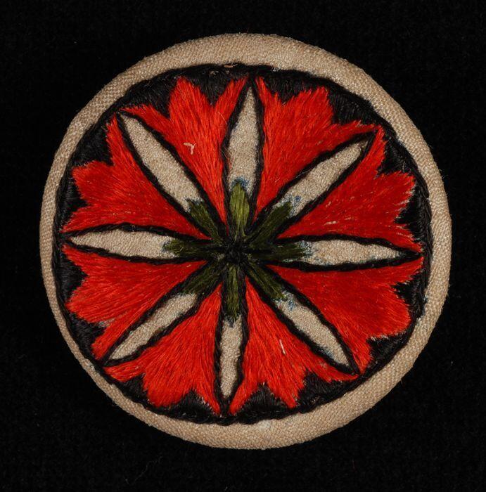 Ronde broche met geborduurd ornament in rood en zwart op champagnekleurig zijde oefening