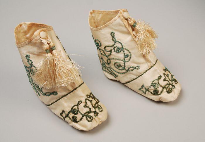 Witte zijdesatijnen babylaarsjes met knoopsluiting met daaraan kwastjes, soutache geborduurd met…