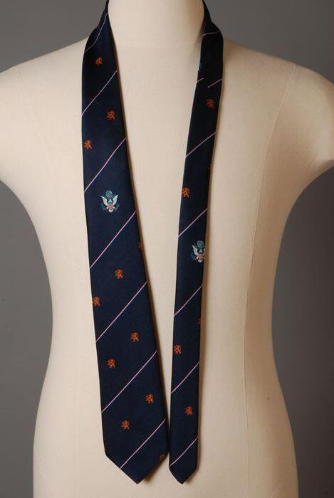 Stropdas, zelfbinder, van zijde(?), donkerblauw met diagonale rood/wit/blauwe strepen met emblemen