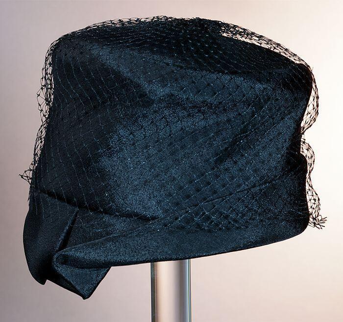 Toque, zwart katoen met stolpplooi in asymmetrische rand, voile op en over de platte bol