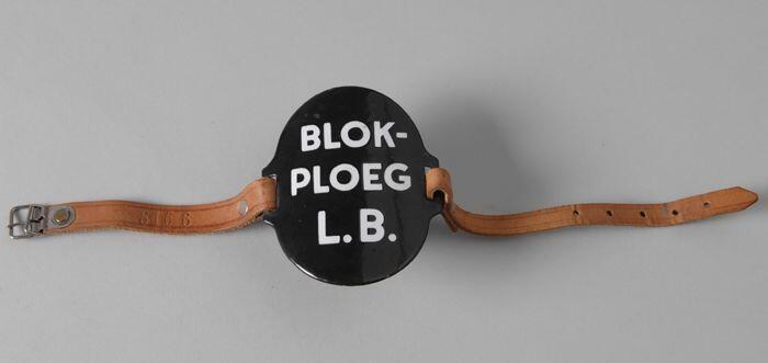 Ovaal zwart-geëmailleerd armschildje met "BLOK-PLOEG L.B.", met leren riempjes aan weerszijde