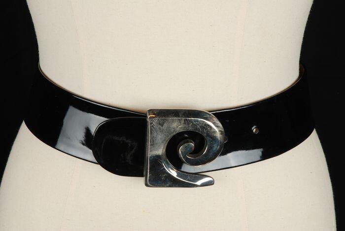 Iets rondlopende brede ceintuur van zwart kunststoflakleer met zilverkleurige metalen gesp met krul…