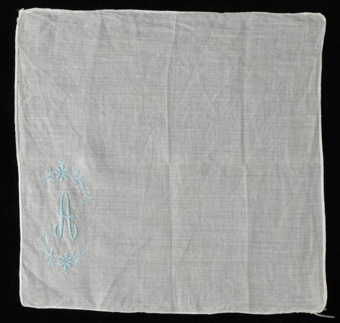 Vierkante wit batisten zakdoek met in één hoek geborduurd monogram tussen bloemranken in lichtblauw…