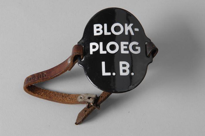 Ovaal zwart geëmailleerd armschildje met "BLOK-PLOEG L.B.", met leren riempjes aan weerszijde