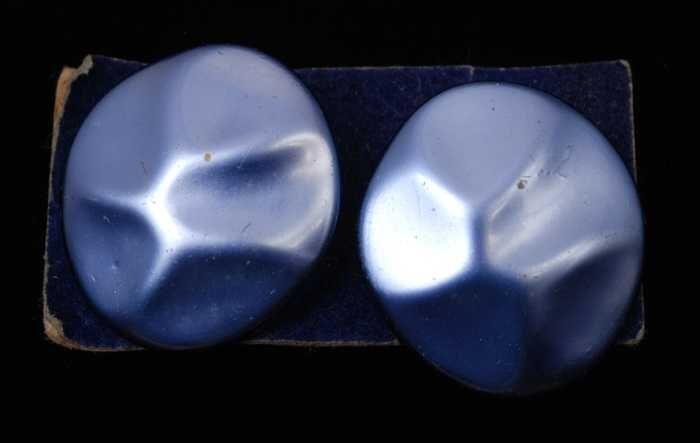 Paar oorbellen, clip met platte ovale gedeukte knop van blauw plastic met paarlemoerglans, op blauw…