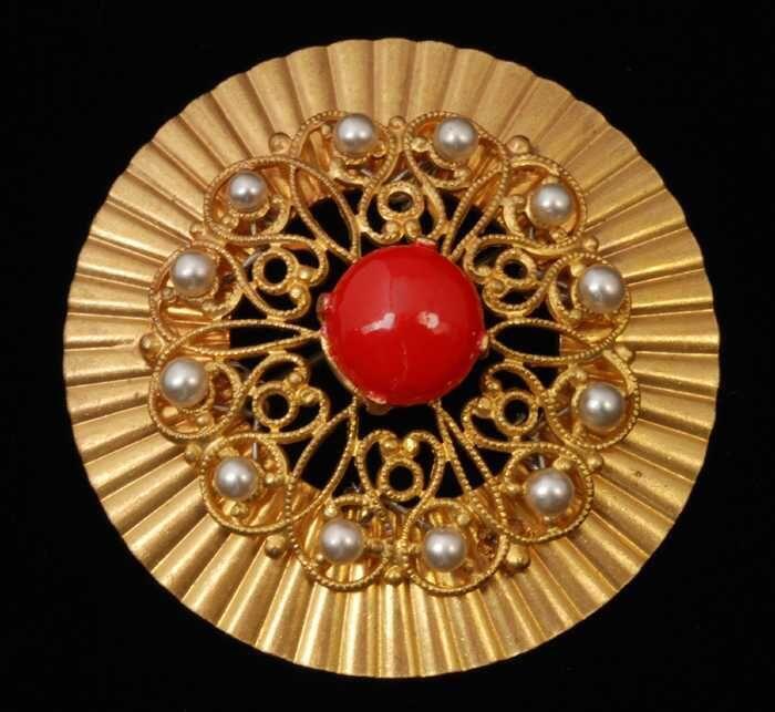 Ronde broche, goudkleurig metaal met filigrein waarop imitatiepareltjes en een rood geverfde 'steen…