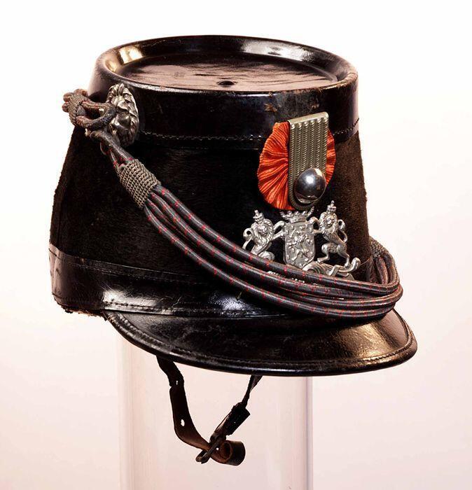 Sjako van zwart haarvilt, zwart lakleer, zilverkleurig embleem met Rijkswapen, leeuwenkophaken