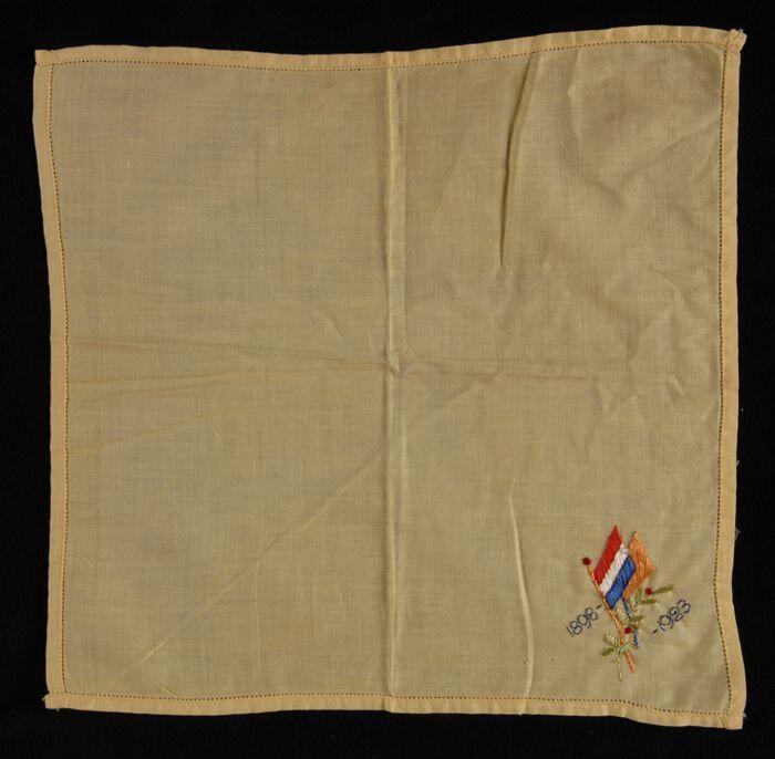 Vierkante gele herinneringsdoek, met borduursel in één hoek, Nederlandse driekleur en oranje vlag…