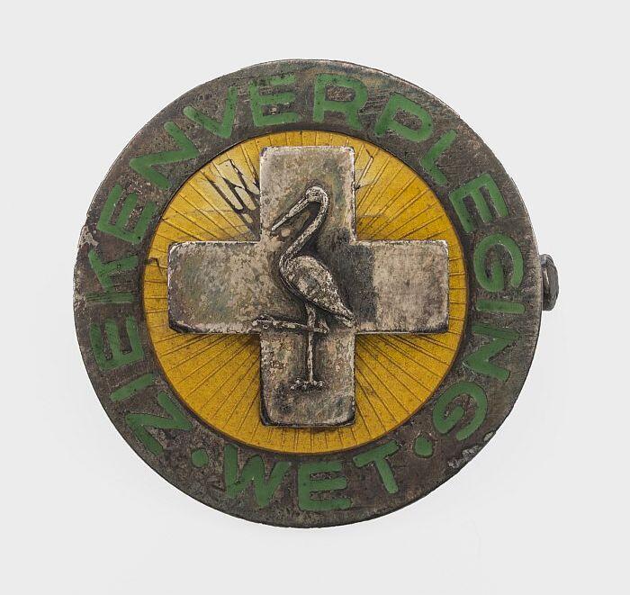 zilveren verpleegsterinsigne met emaille, groene tekst "ziekenverpleging wet" op een geel fond een…