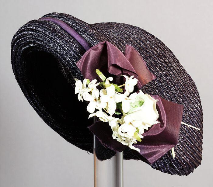 Strohoed zonder rand, donkerblauw bandstro met paars satijnen strik en wit zijde bloemen corsage