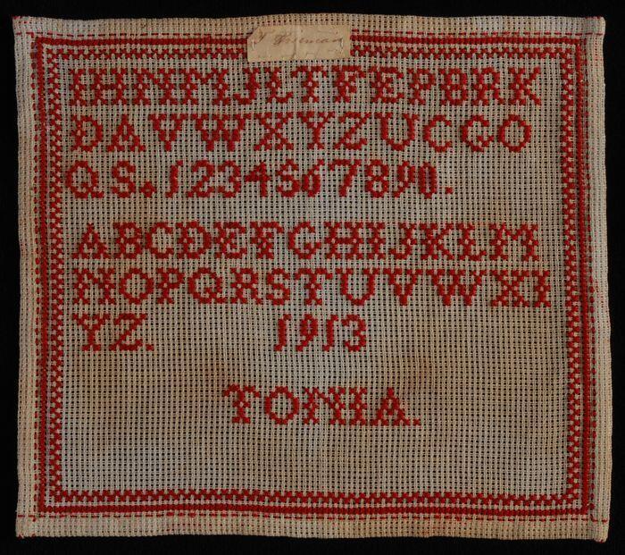 Letterlap met rood kruissteekborduursel op grof wit linnenstramien, oefening, gemerkt "Tonia"