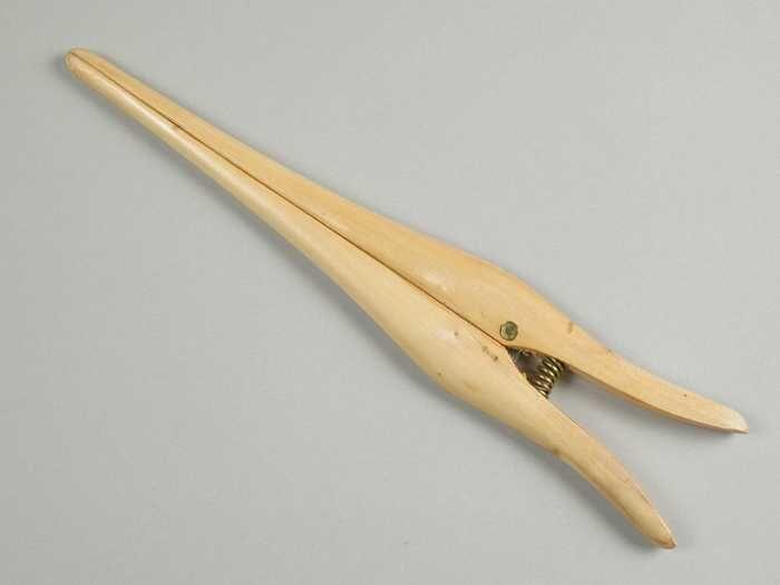 Handschoenrekker van blank gelakt hout twee spits toelopende poten met metalen veer
