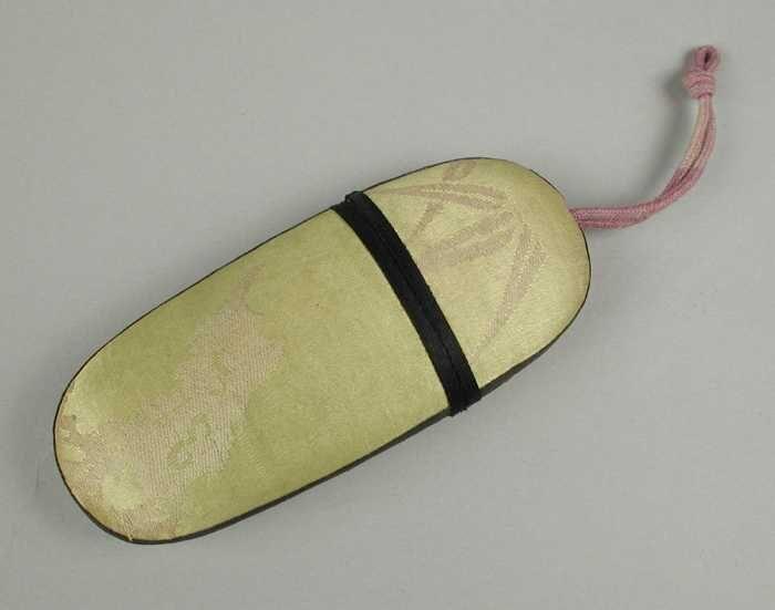 Brillenkoker van karton bekleed met geel zijde met zwarte biezen en een lila koordje