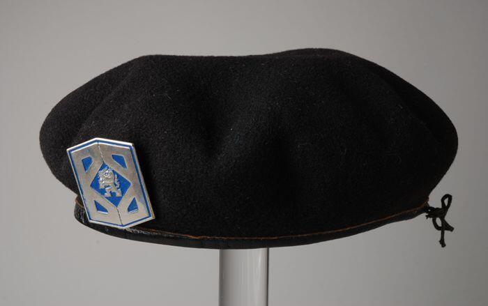 Baret van zwart vilt met entree van zwart leer, met zeshoekige metalen speld waarop de gestileerde…