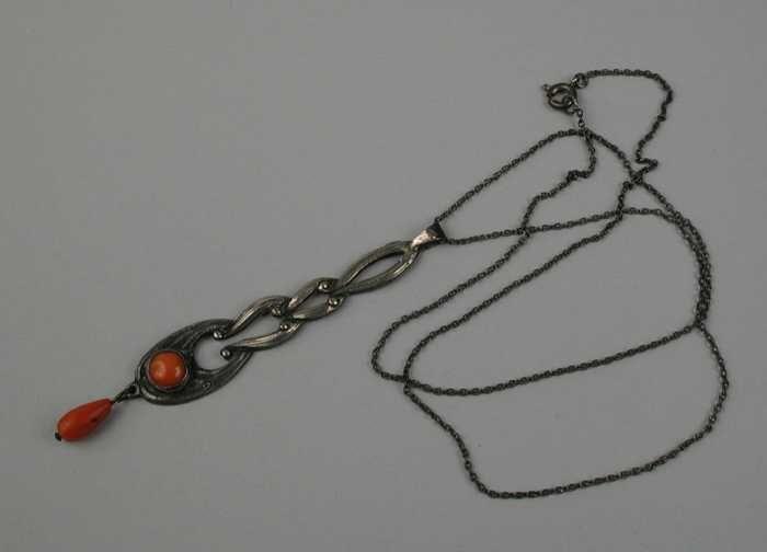 zilveren ketting met lange hanger van vier in elkaar grijpende krullen, onder zettin met steentje…