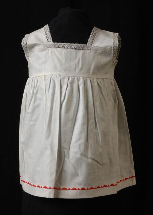 Babyjurk, mouwloos schortmodel van wit katoen 'Femifra' met rode afwerking, nylonkant langs hals en…
