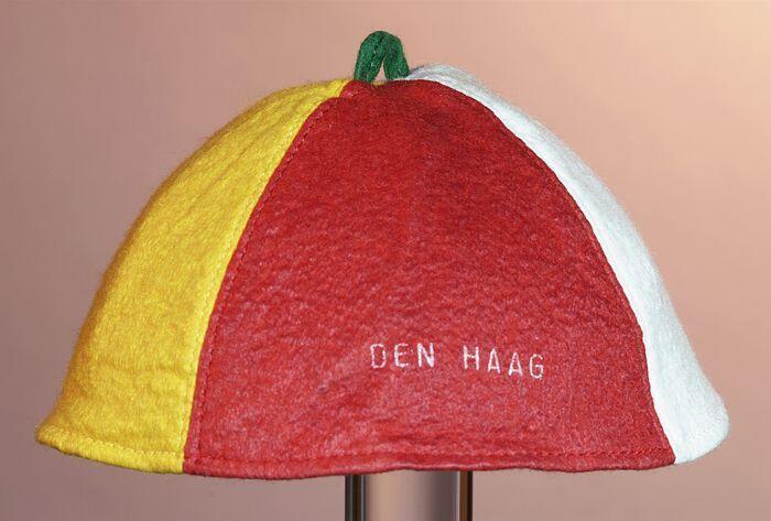 Rond vilten vakantiemuts (?) van vier delen rood, wit, blauw en oranje met groen lusje middenop, in…