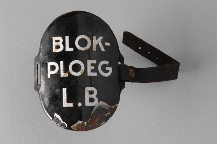 Ovaal zwart geëmailleerd armschildje met "BLOK-PLOEG L.B.", met één leren riempje