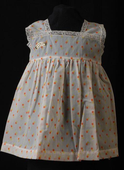 Babyjurk, mouwloos schortmodel van transparant nylonmet gele en oranje stippen, 'Femifra'