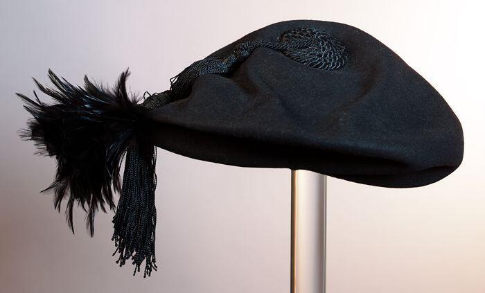 Zwarte vilten baret met garnering van zwarte veren en zwart koord met kwast