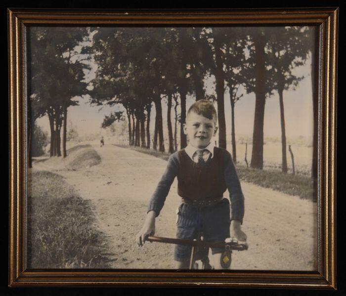 Ingekleurde foto achter glasin goudkleurige lijst, jongentje op een fiets op een bomendijk