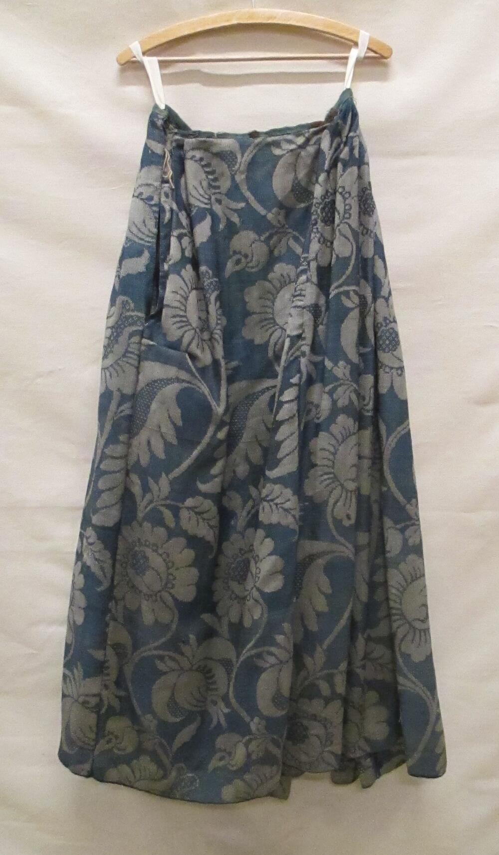 Rok van blauw met beige wollen damast met grote florale motieven. Voorpand vlak aan de rokband van…