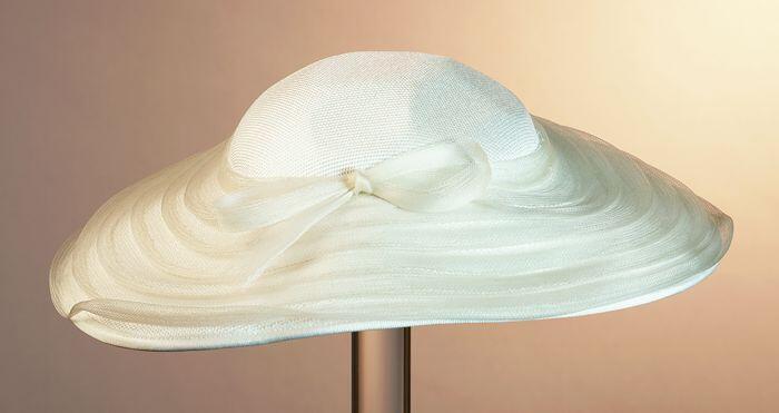 Ovale vrij platte hoed van wit nylonmet garnering van wit kunststofcrine geplooid rondom de bol op…