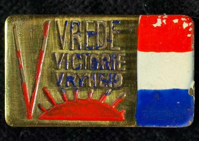 Rechthoekige metalen speldje met "VREDE VICTORIE VRYHEID", oranje V-teken, oranje zon en…