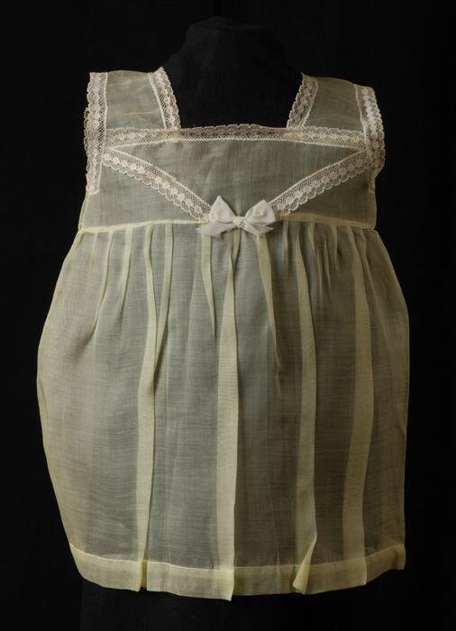 Babyjurk, mouwloos schortmodel van transparant geel nylonmet wit kant, 'Femifra', model "No 20"